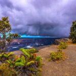 A scenic view of a volcanic landscape with lush greenery and dark clouds overhead.