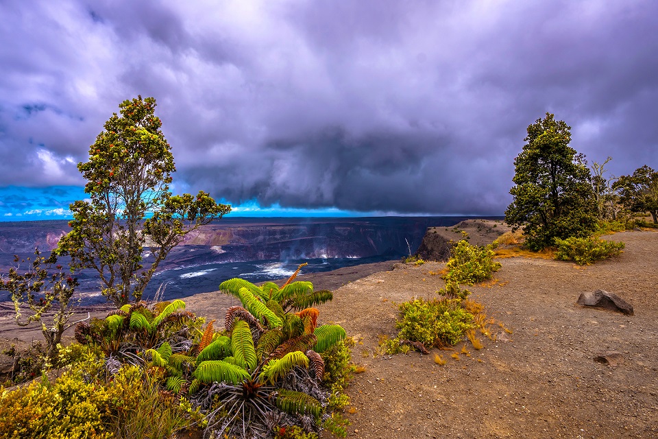 A scenic view of a volcanic landscape with lush greenery and dark clouds overhead.
