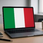 A laptop with the Italian flag displayed on the screen, placed on a desk with a notebook and a coffee mug beside it.
